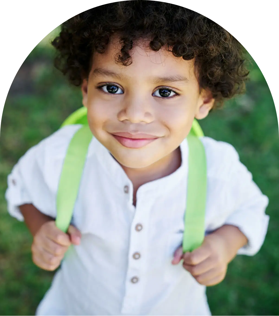 Child smiling with green backpack outdoors.